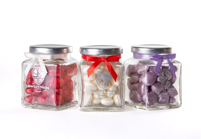 Multicolor candies in glass jars on color wooden background фотография Stock Ado